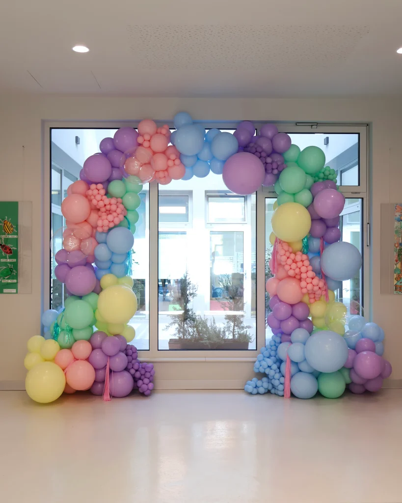 Veliki balonski luk s pastelnim šarenim balonima, ukrašen prozirnim balonima i resicama. Idealan za raskošna i vesela otvorenja te evente