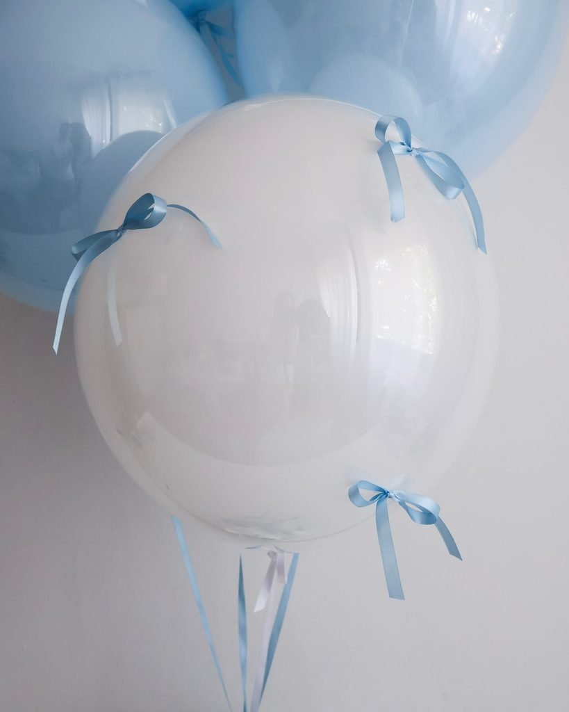 Jumbo bijeli balon na helij obučen u proziran bobo balon ukrašen plavim satenskim mašnama idealan za proslavu rođenja dječaka.